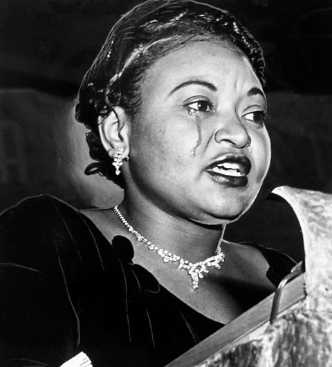 A photograph of Mamie Till speaking. There are tears running down her face.