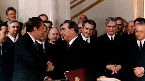 A photograph of President Nixon and Leonid Brezhnev shaking hands as a group of men look on