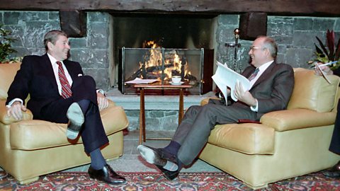 A photograph of President Regan and Soviet leader Mikhail Gorbachev sitting in armchairs in front of a fire, laughing together