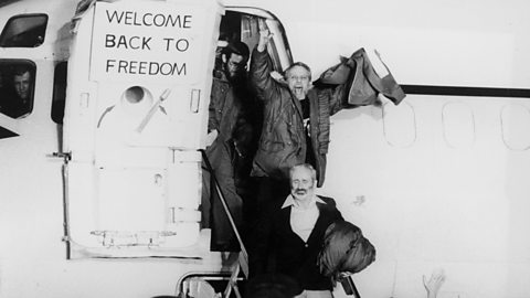 Three men disembarking from a plane which has the sign 'Welcome back to freedom'. One looks to be emotional and another is shouting with joy