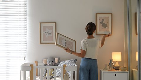 A woman hanging frames in a baby's nursery.