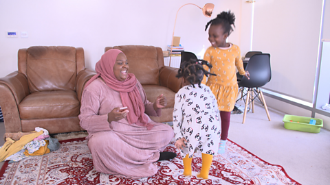 Mum sitting on the floor in the living room, dancing with her two young daughters.