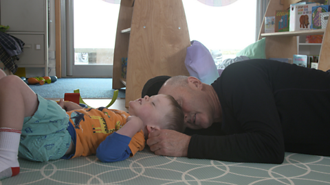 Young boy lying on the floor with his grandpa, both have their eyes closed and are breathing deeply.