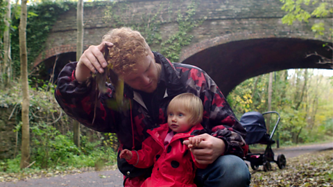 Dad and daughter are outside on a walk looking at a leaf together.