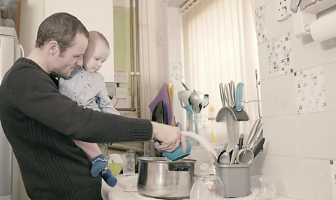 Dad and son washing dishes together at the sink.