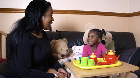 Mum and daughter have a pretend tea party with teddy bears at home