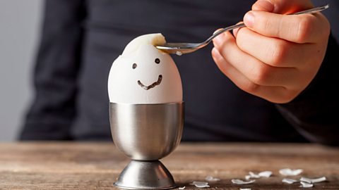 A child eating a boiled egg which has a happy face drawn on the side of the shell 