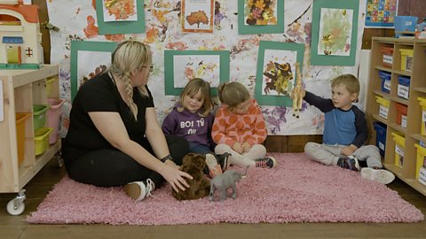 Nursery Worker Lisa sits on the floor in her childcare setting with 3 children.