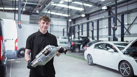 Apprentice holding a catalytic converter from a car