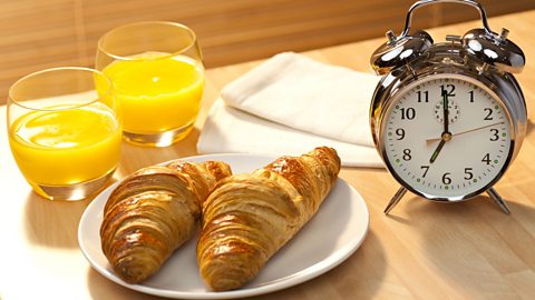 Could an early breakfast mean a longer life? two glasses of juice, a plate with two croissants and a traditional alarm clock showing it's 7am