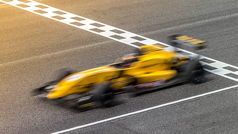 A yellow formula one car passing over the finish line. The photo is is blurry with motion blur.