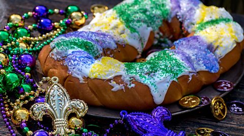 Beads and other Mardi Gras decorations surround a decorated king cake