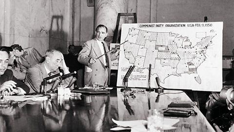 Joseph McCarthy pointing at a map of the USA, while addressing a room of people