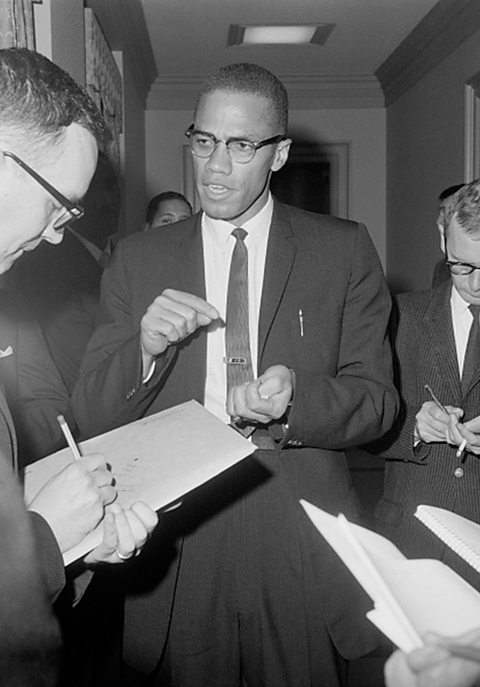 Malcolm X being interviewed by reporters in a corridor