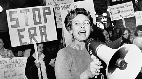 Phyllis Schlafly speaking into a megaphone with a group of people holding up signs behind her