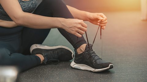 A white person tying their shoelaces on a pair of black trainers