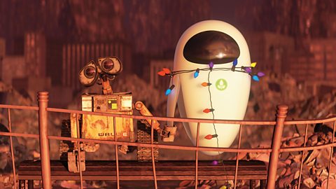 A still from the animated film WALL-E. Two robots hold hands while surrounded by rubbish. One is oval in shape, white and futuristic looking. The other is square with tracks for feet and is made of rusting metal.