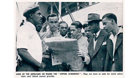 A black and white photograph of passengers on the Empire Windrush, who are looking at a newspaper.