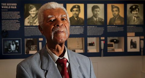 A photograph of Sam King, who is standing in front of a display board in a museum.