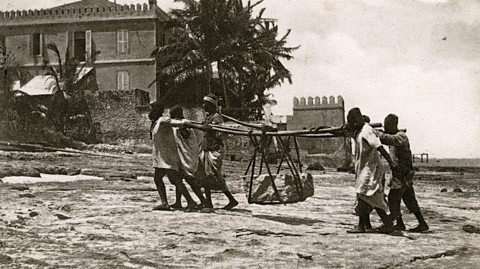 A black and white photograph of indentured labourers carrying stone in Zanzibar.