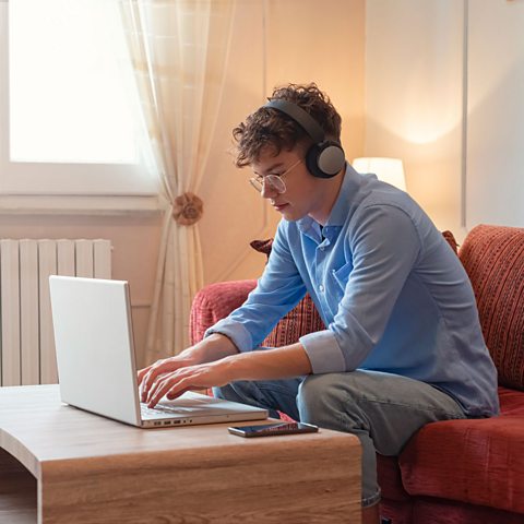 A young person wearing headphones and typing on a laptop.