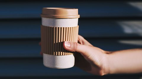 A hand holding out a reusable coffee cup. 