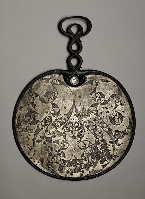 Bronze mirror with a clover-leaf pattern. It is part of the British Museum's collection.