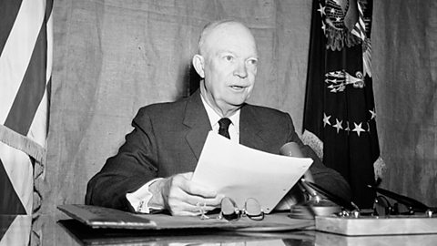 A photograph of President Eisenhower speaking into a microphone with a piece of paper