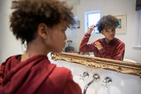 A boy examines his hair in the mirror