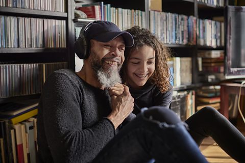 A dad and his child sit together in front of a CD shelf