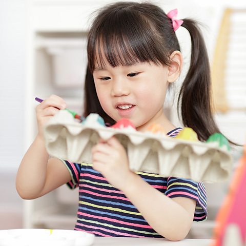 A young girl with black hair is decorating egg cartons with paint.