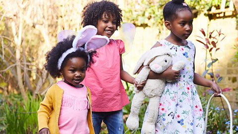 3 young girls are in their garden doing an easter egg hunt. One is wearing bunny ears.