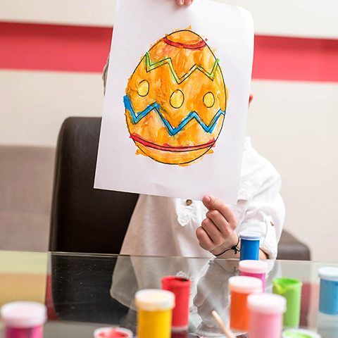 A boy holds a picture of a hand-drawn Easter egg in front of his face.