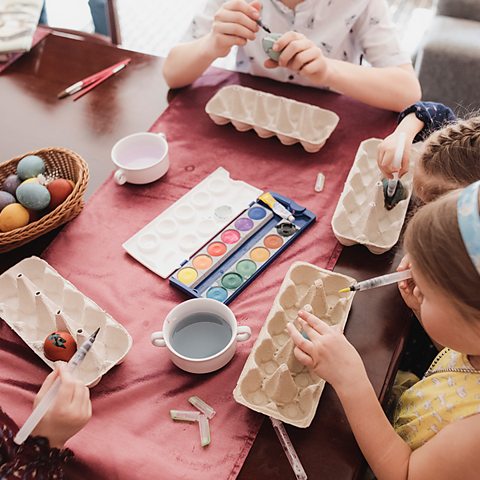 A group of children sit at a table and decorate eggs together for Easter.