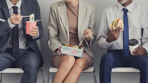 people in suits eating a variety of lunches: a pot of noodles, salad and burger