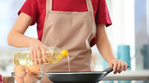 someone pours oil into a frying pan (can't see their face)