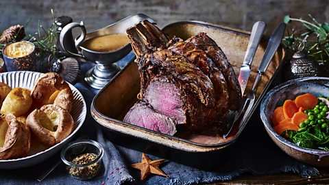 roast beef in a tray served with Yorkshire puddings, gravy, peas and carrots