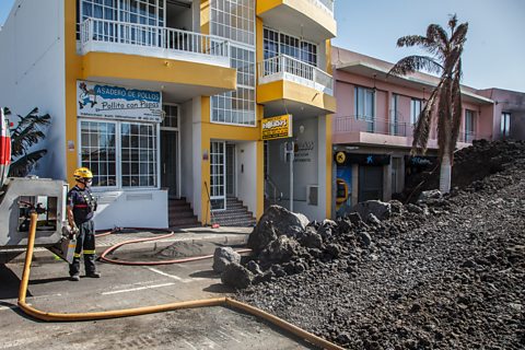 A fireman stands in a tidy area next to a large pile of rubble