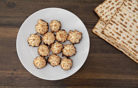 A white plate with some chocolate covered coconut macaroons and Matzo bread to the side.