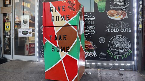 A fridge-freezer sits outside a shop with writing on it saying 'give some, take some'