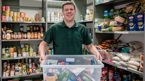 A man works in a food bank with shelves surrounding him 