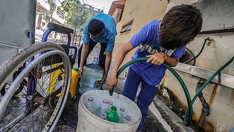 Palestinian children fill plastic bottles and jerrycans with drinking water