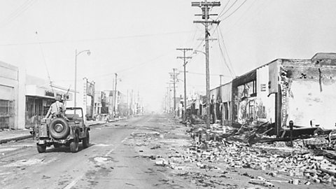 A photograph of solider riding in a jeep through a heavily damaged street