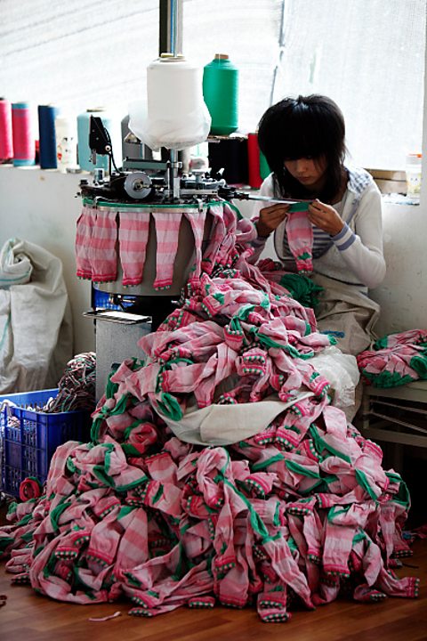 A woman sat on a bench with a large pile of socks in front of her whilst she makes them.