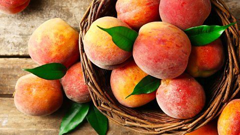 A wooden basket filled with peaches on a wooden table