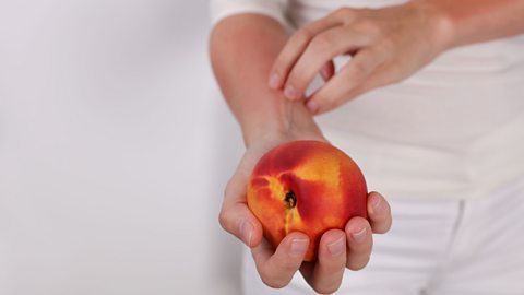 someone scratches their arm while holding a peach