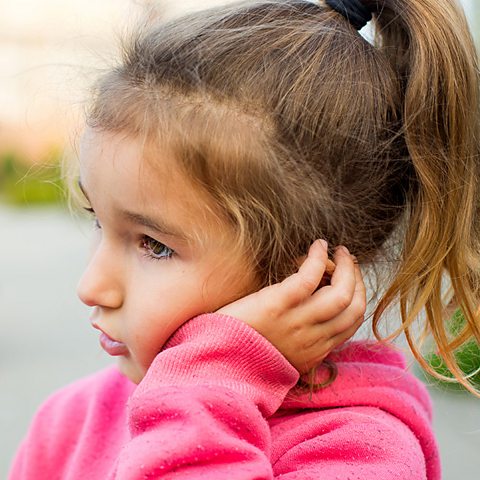 Glue Ear - A girl in a pink jumper is holding her ear as if she is in pain.