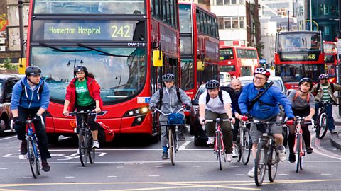 A group of cycles riding on the road in front of a red double decker bus in London.