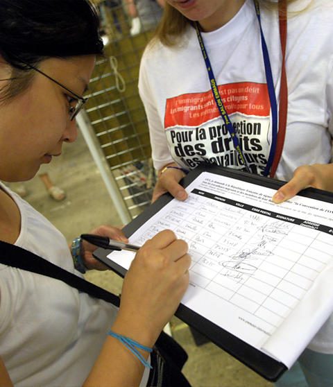 Two people - One holding a piece of paper on a clipboard with a slogan on their t-shirt, the other signing the piece of paper