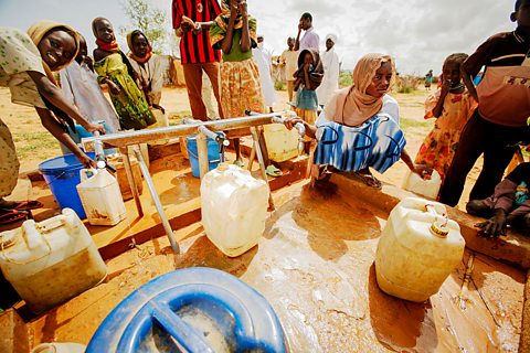 A group of people on a sandy ground collecting plastic containers of water.